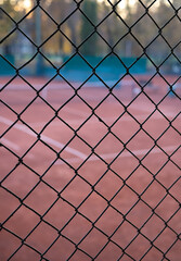 abstract tennis court view through a diamond wire mesh fence at sunset or dusk. shallow depth of field, focusing on the foreground netting