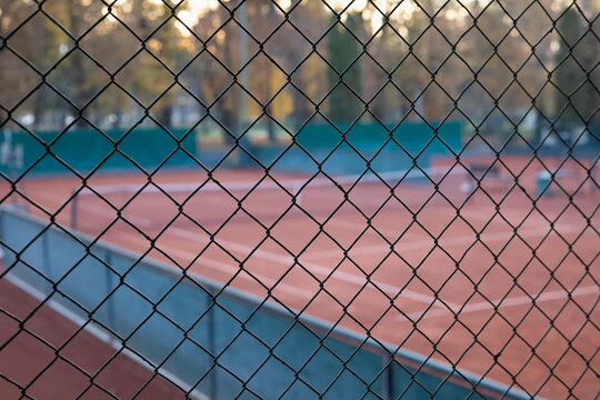 abstract tennis court view through a diamond wire mesh fence at sunset or dusk. shallow depth of field, focusing on the foreground netting