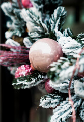 Elegant Christmas pink ornament on snow covered evergreen branches with a soft winter atmosphere. Close-up. Selective focus.