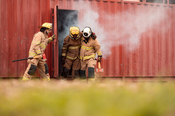 A team of firefighters evacuates an injured colleague from a smoke-filled training structure