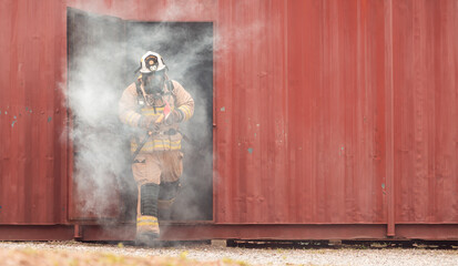 A firefighter in full protective gear runs out of a smoke-filled structure carrying an emergency axe