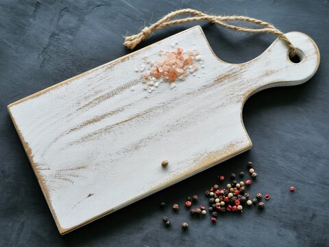 Rustic white cutting board with himalayan pink salt and peppercorns on dark table