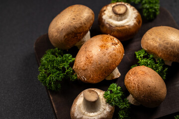 Fresh cremini mushrooms and parsley on dark cutting board arranged for cooking