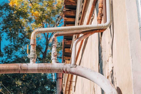 Old, weathered industrial gas pipes running along an exterior building wall, showing rust and corrosion under a bright sky