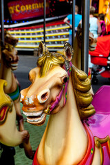 Close-up photo of a worn vintage carousel horse at an amusement park, showing chipped paint and vibrant colors. People and lights softly blurred in the background. © Kerstin H Lofgren
