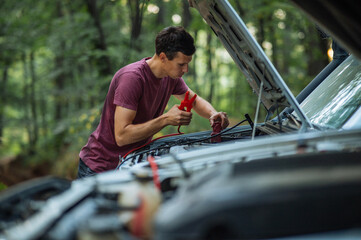 Man Jump-Starting Car in Nature with Jumper Cables.