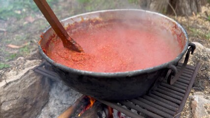 Preparing classic homemade Italian tomato sauce for pasta and pizza in a large pan outdoors over a wood fire. Stirring with a wooden spoon a hot dish that is bubbling and steaming - Powered by Adobe