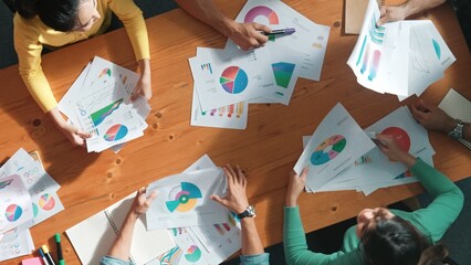 Top down view of start up business team holding paper while discussing about financial idea. Aerial view of smart diverse people brainstorming idea while looking at stock market statistic. Symposium.