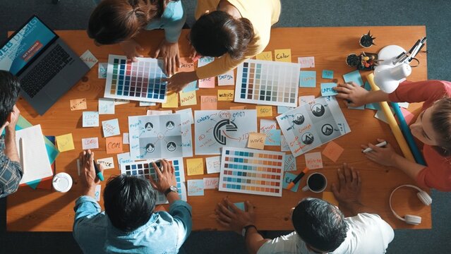Top down view of designer compare color palettes with laptop and design product. Aerial view of marketing team working together to choose color while discussing about logo graphic design. Symposium.