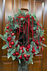 A beautifully decorated wooden door with a Christmas wreath with red bubles and beads.