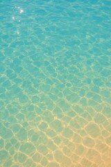 Obraz premium Crystal clear ocean water with sunlit ripples and sandy bottom creates a serene, inviting tropical paradise escape.