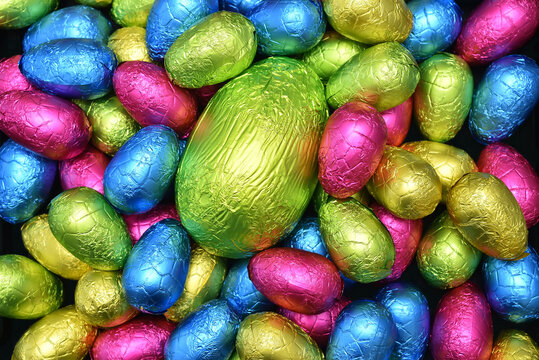 Pile  of colourful foil wrapped chocolate easter eggs in pink, blue, yellow and lime green with a large green egg in the middle.