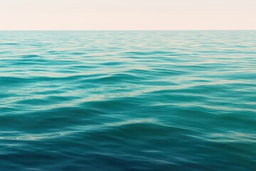 Obraz premium Tranquil turquoise ocean waves gently ripple under a soft, serene sky, evoking peace and boundless natural beauty for your next project.