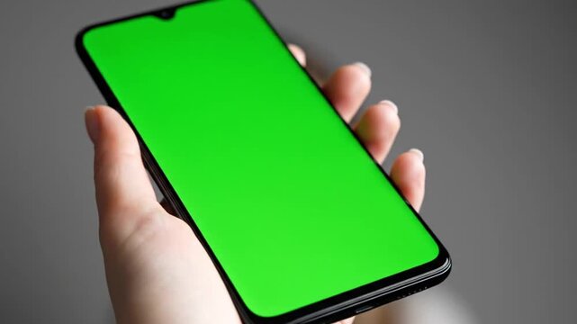 Woman's hand holding modern smartphone with vibrant green screen ready for creative content integration and dynamic visual effects in digital projects