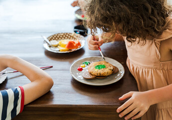 Kids decorating a large round cookie with edible paints and brushes during a tropical Christmas creative activity, painting festive designs like trees and ornaments, fun DIY holiday food art workshop