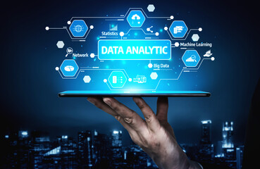 A hand holds a digital tablet displaying futuristic data analytic concepts and graphics against a stunning night cityscape, representing technology and innovation. Tessel