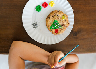 Kids decorating a large round cookie with edible paints and brushes during a tropical Christmas creative activity, painting festive designs like trees and ornaments, fun DIY holiday food art workshop