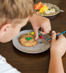 Kids decorating a large round cookie with edible paints and brushes during a tropical Christmas creative activity, painting festive designs like trees and ornaments, fun DIY holiday food art workshop