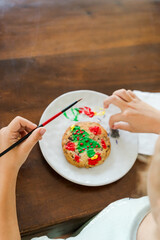 Kids decorating a large round cookie with edible paints and brushes during a tropical Christmas creative activity, painting festive designs like trees and ornaments, fun DIY holiday food art workshop