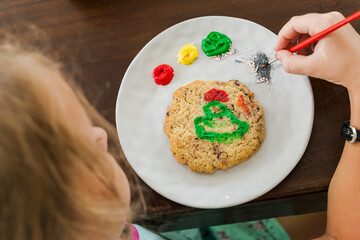 Kids decorating a large round cookie with edible paints and brushes during a tropical Christmas creative activity, painting festive designs like trees and ornaments, fun DIY holiday food art workshop