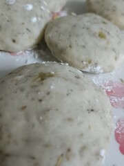 Raw, pale dough patties arranged on a light surface, showing a coarse texture with grains or spices. These uncooked tikki-style discs resemble Indian snack dough prepared for frying or baking.
