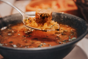Spoon lifting a piece of meat from a bowl of hot Georgian soup