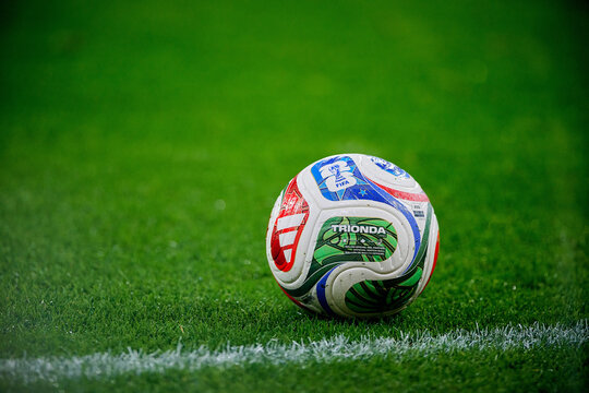 Single match ball Trionda on green turf near the touchline with broad copy space&mdash;clean, colorful detail before play.