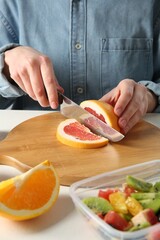 Making fruit salad. Woman cutting grapefruit at white table, closeup