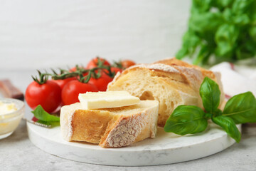 Slices of baguette with butter, basil and tomatoes on light grey table, closeup. Space for text
