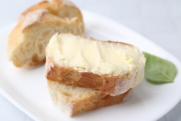 Slices of baguette with butter and basil on white table, closeup