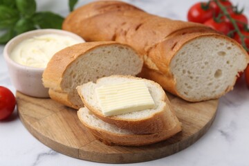 Cut baguette with butter, basil and tomatoes on white marble table, closeup