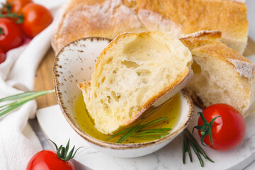 Tasty baguette served with oil, tomatoes and rosemary on table, closeup