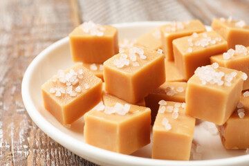 Tasty caramel candies with salt on color wooden table, closeup