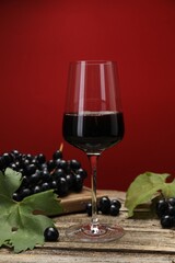 Red wine in glass, grapes and green leaves on wooden table against color background, closeup