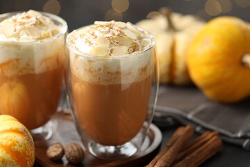 Tasty pumpkin latte with whipped cream and spices on black table against blurred lights, closeup