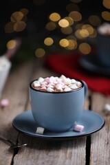 Tasty cocoa with marshmallows on wooden table against blurred Christmas lights, closeup