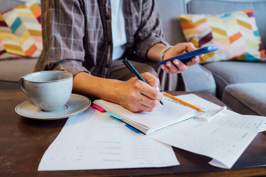 Middle aged woman reviewing expenses, managing personal finances on smartphone mobile app while sitting on couch with coffee in cozy living space. finance planning, financial balance check, budgeting