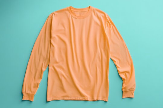 A folded peach-colored long-sleeved shirt lies flat against a bright turquoise background for a stylish and simple product presentation.