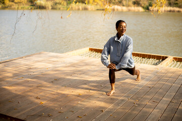 Korean woman practicing lunges by the serene lakeside during a sunny afternoon