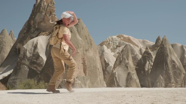 Cheerful dancing woman traveler moonwalking against backdrop of rock formations in mountain valley of Cappadocia