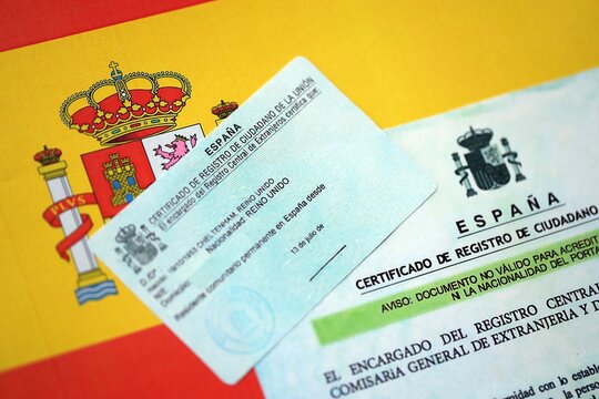 Citizenship or naturalization certificate document and card on flag of Spain close up