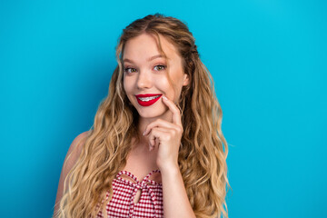 Glamorous young woman with blonde hair smiling in a red checkered top against a blue background...