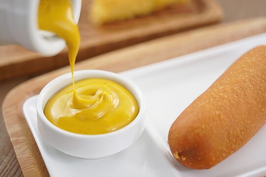 Close-up corn dog with crisp sun-gold batter on a pristine white plate, inviting.