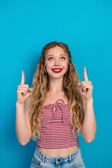 Young glamorous girl with long blonde hair wearing red checkered top and jeans pointing up against...