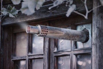 Exhaust pipe protruding from a broken window in a vintage wooden house