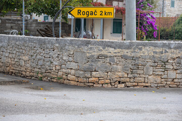 Rogac Road Sign Amid Lush Greenery and Stone Wall Backdrop, Solta, Croatia