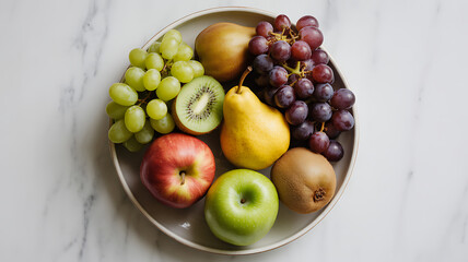 Overhead shot of a plate filled with fresh and colorful fruits, including apples, pears, grapes, and kiwis, arranged on a marble surface