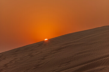 The sun rising on the pristine and untouched red dunes in the desert near Dubai
