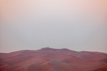 People standing on the red dunes in the desert near Dubai waiting for the sunrise