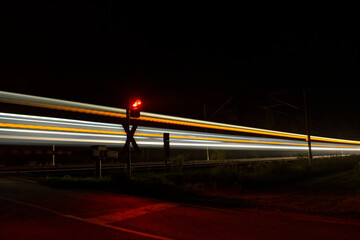 Leuchtspur eines Zuges der in der Nacht an einem Bahn&uuml;bergang vorbei f&auml;hrt